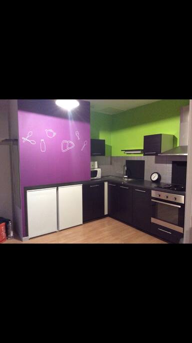 Cuisine avec micro onde, frigo, congélateur, cafetière, four, plaques de cuisson et assiettes/couverts.