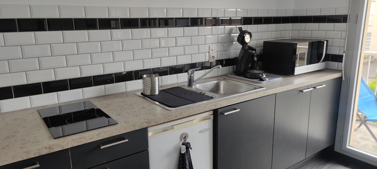 The kitchen area features sleek black and white subway tile backsplash. Modern appliances are visible, including a microwave and coffee maker. A stainless steel sink is situated beneath a well-lit window, with ample counter space and cabinetry enhancing functionality.