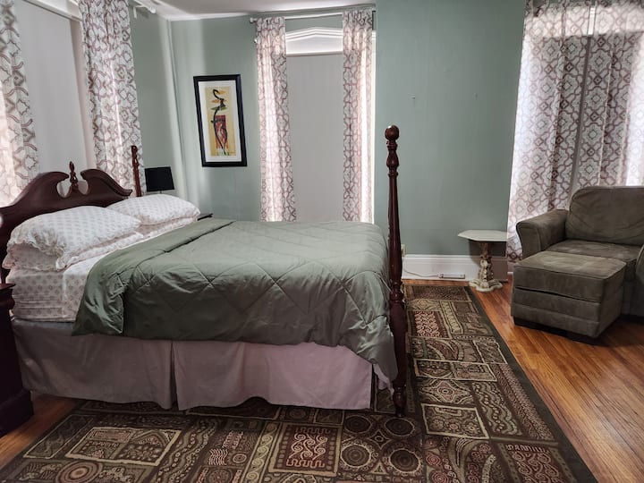 Dormitorio grande con una televisión inteligente y una silla cómoda.