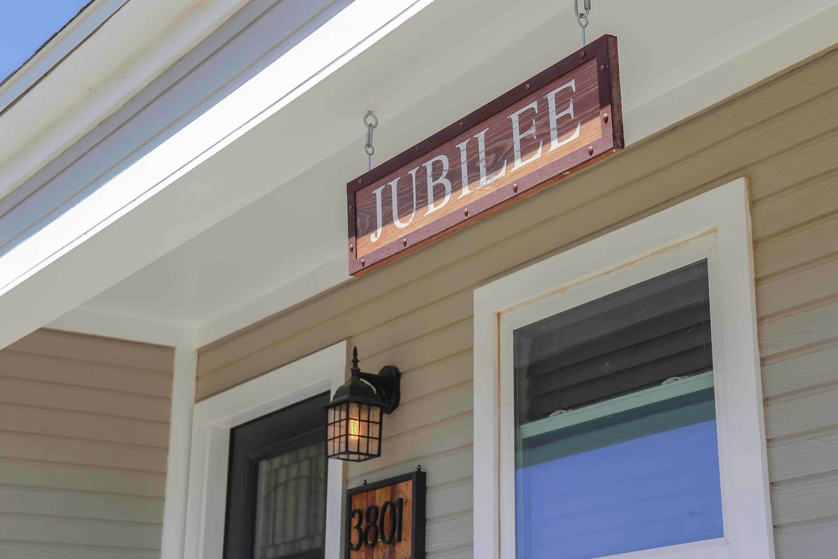 The entrance features a wooden sign labeled 'Jubilee,' elegantly mounted above the door. A light fixture with a warm glow is positioned beside the entrance, illuminating the inviting atmosphere of the front porch.