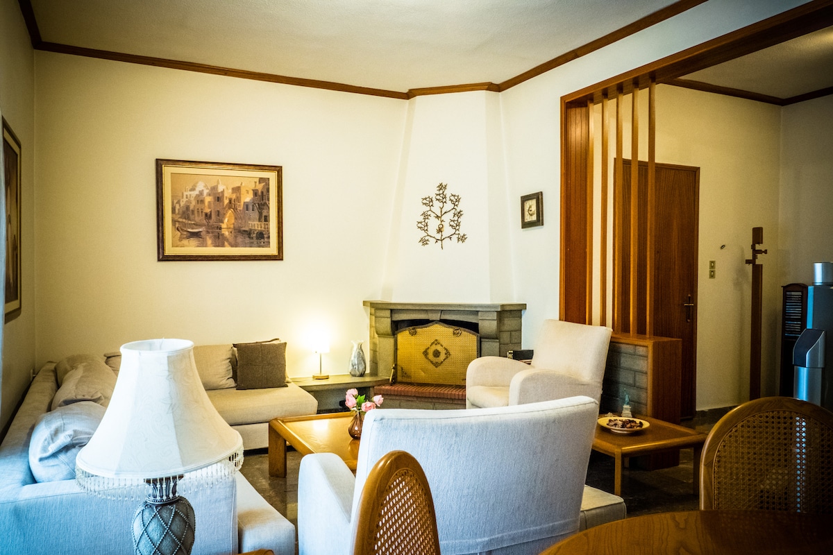 A welcoming living space is presented with a comfortable sofa and armchairs arranged around a wooden coffee table. A decorative fireplace serves as a focal point, and wall art adds character. Soft lighting enhances the room's inviting atmosphere, complemented by natural light from a nearby window.