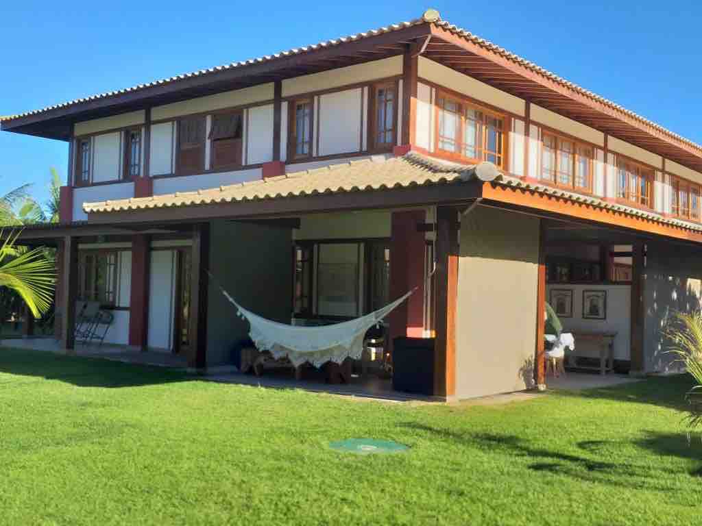 The exterior of the two-story apartment features a blend of wood and glass, creating an open and airy feel. A hammock hangs gracefully in the shaded area, surrounded by well-maintained green grass. The design emphasizes natural light with large windows throughout.