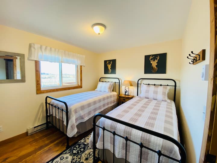 Dormitorio número tres. Tiene dos camas individuales extra largas, mesita de noche con lámpara, mesa pequeña y juguetes para niños y libros en el armario.