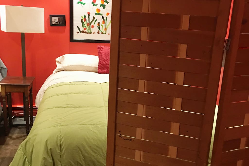 Comfortable queen bed behind a privacy screen in basement bedroom.