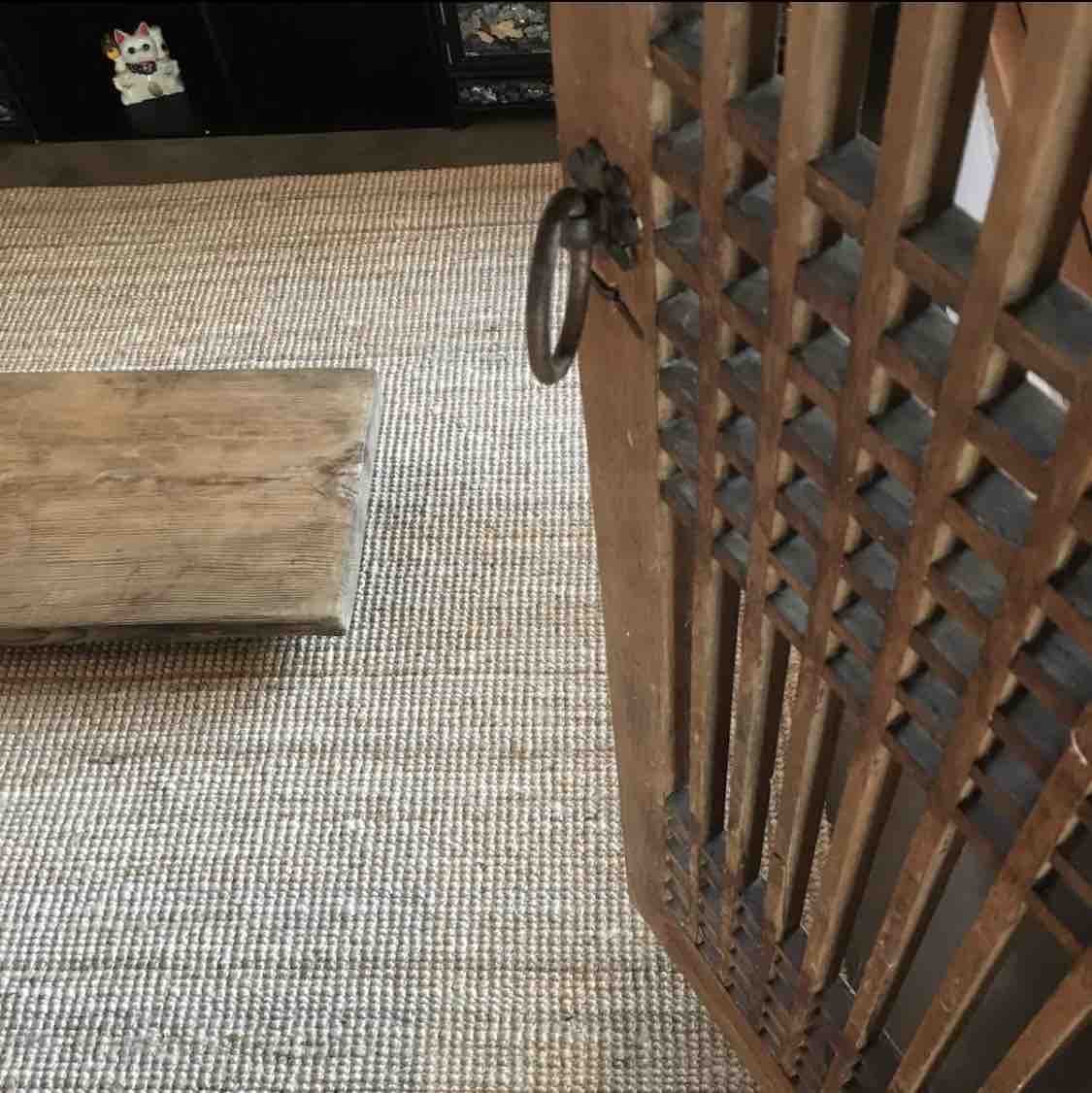 A wooden door with decorative grilles is captured alongside a rustic wooden bench. The floor is covered with a textured woven mat, creating a cozy ambiance. A glimpse of a black cabinet can be seen in the background, adding to the harmonious space.