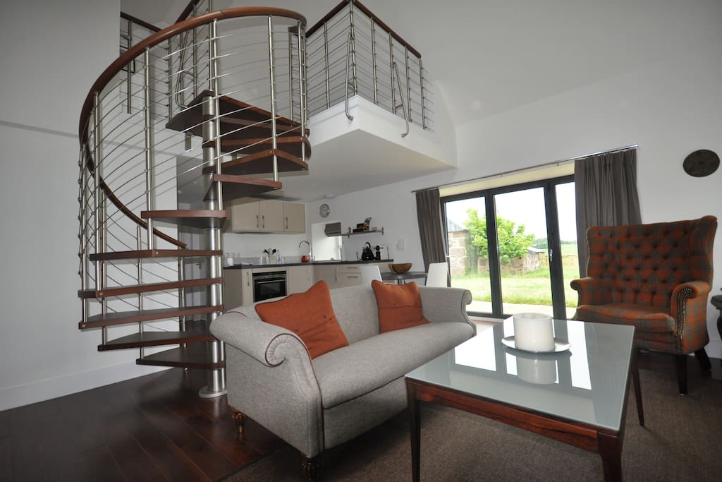 Open lounge with kitchenette and spiral staircase to sitting area and books.