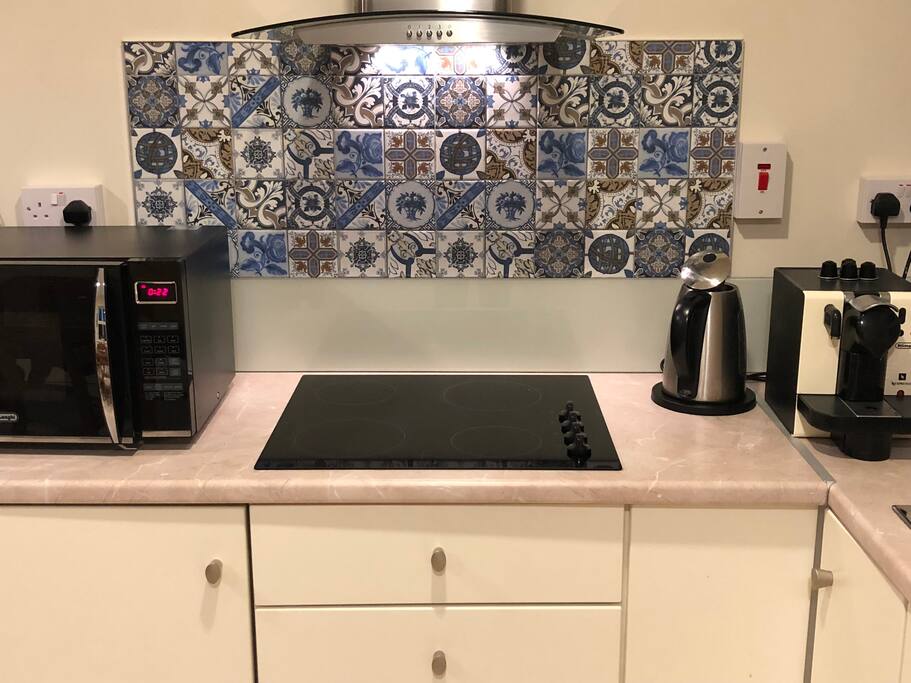 Modern kitchen with electric hob, microwave combo oven, Nespresso coffee machine, fridge, kettle and toaster.