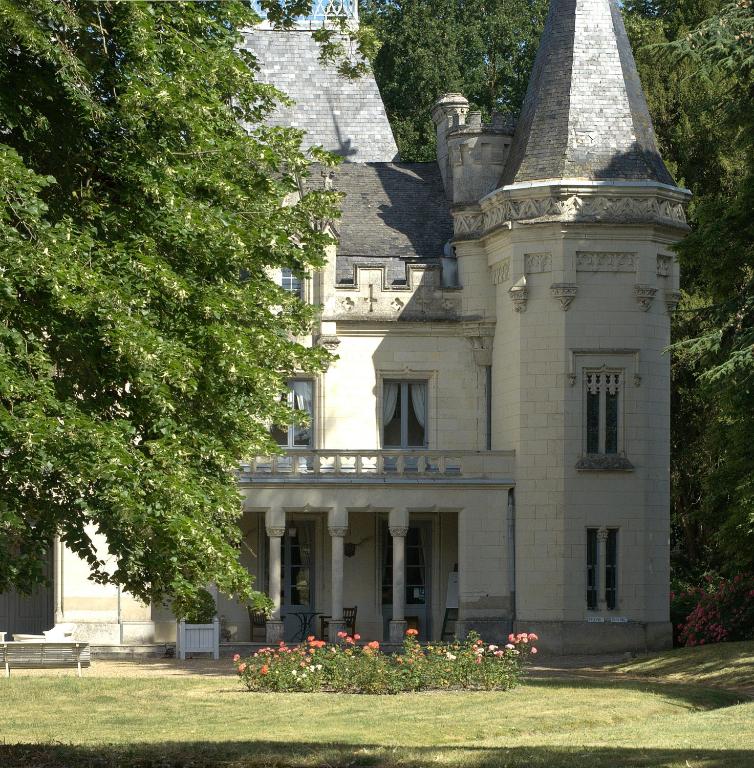 A charming château features elegant stone architecture and distinctive turrets. Surrounding gardens include manicured lawns and rose bushes. Large windows and a balcony provide views of the exterior, inviting natural light into the building.