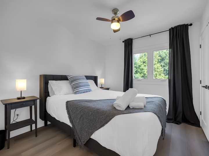 Chambre queen size confortable avec tables de chevet et lampes avec prises de recharge, placard et ventilateur du plafond.