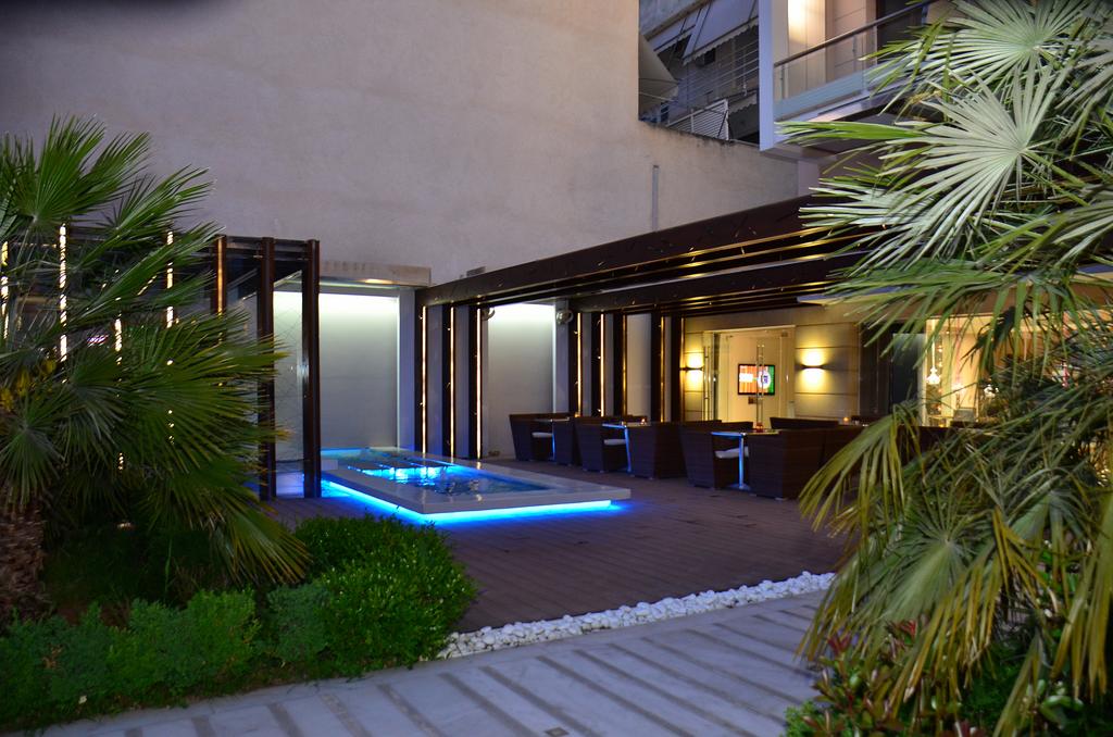 An outdoor lounge area features modern seating arranged around a sleek, illuminated water feature. Lush greenery lines the space, and soft lighting enhances the contemporary architecture, creating a welcoming environment for relaxation. The area is partially enclosed for added comfort.