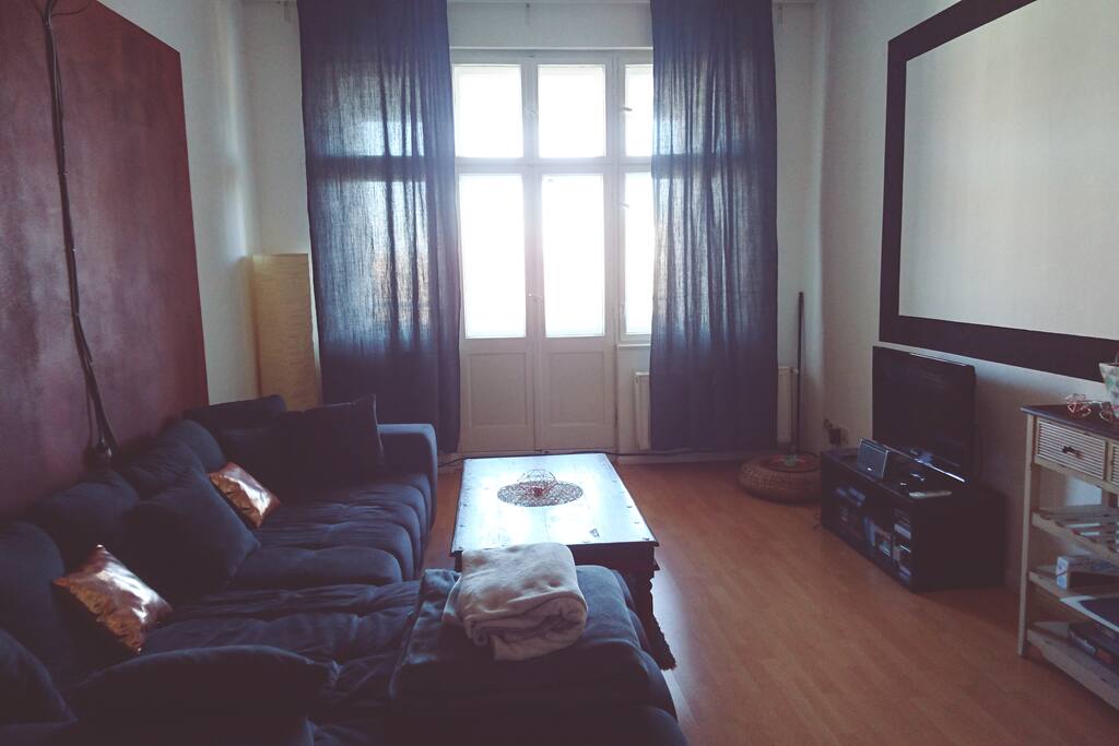 Gemütliches Wohnzimmer mit TV, riesiger Wohnzimmercouch und Blick auf den Balkon.