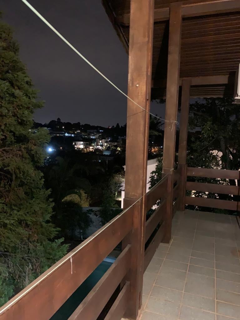 A wooden balcony is shown, with a low railing providing a clear view of the nearby landscape. Soft lights from distant buildings are visible against the night sky, creating a serene ambiance in the outdoor space.
