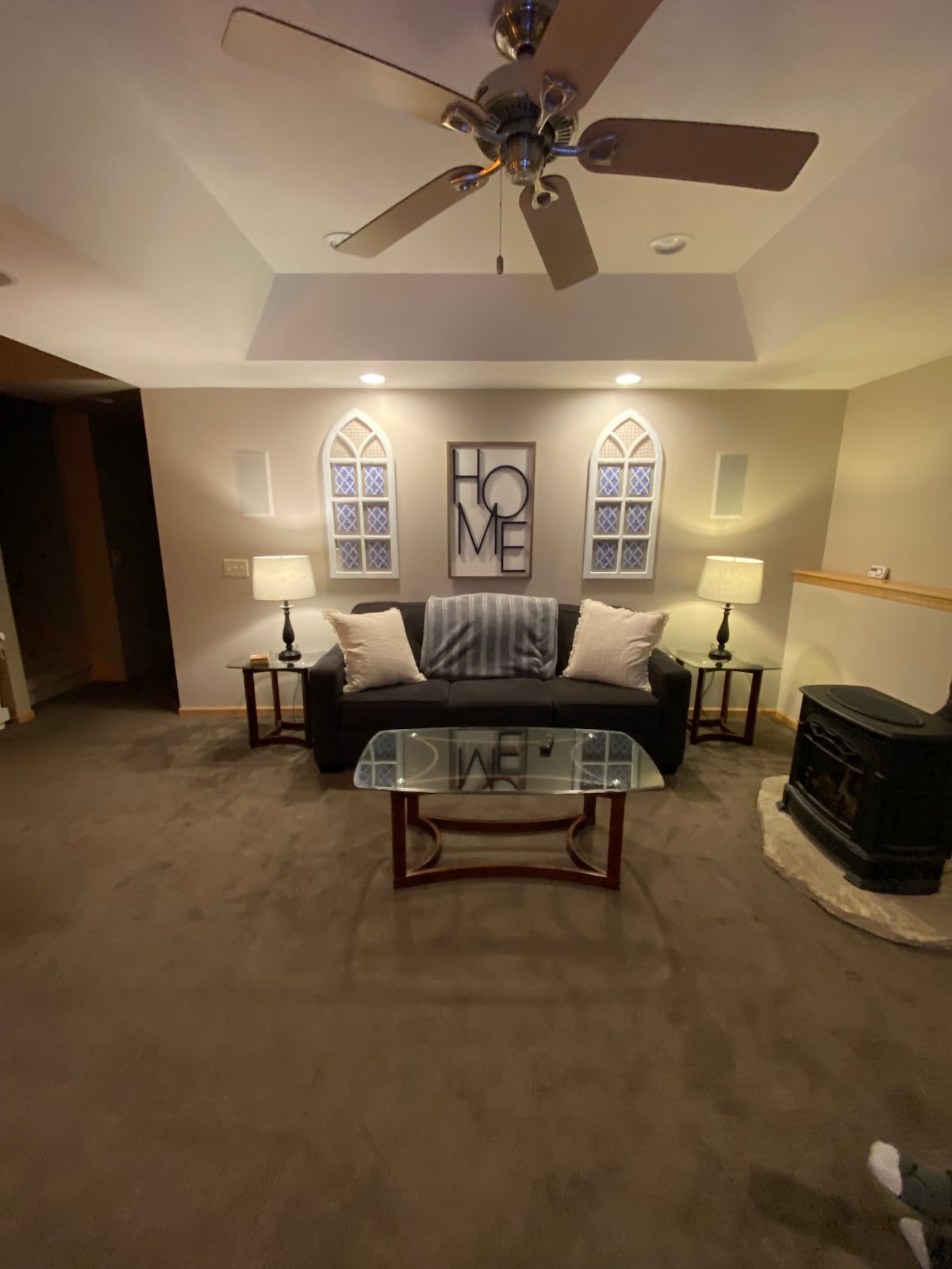 A welcoming family room is featured with a comfortable sofa adorned with decorative pillows. A glass coffee table sits in front, accompanied by two lamps that provide soft lighting. A gas fireplace adds warmth, and light fixtures are mounted above the seating area.