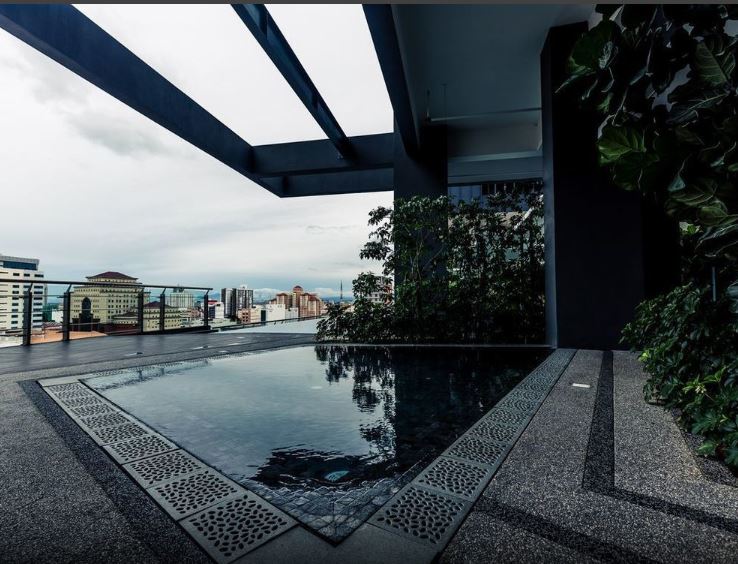 An inviting infinity pool is nestled on the balcony, offering a distinctive view of the city skyline and surrounding greenery. The pool's sleek lines are complemented by modern stone tiles, enhancing the overall elegance of the outdoor space.