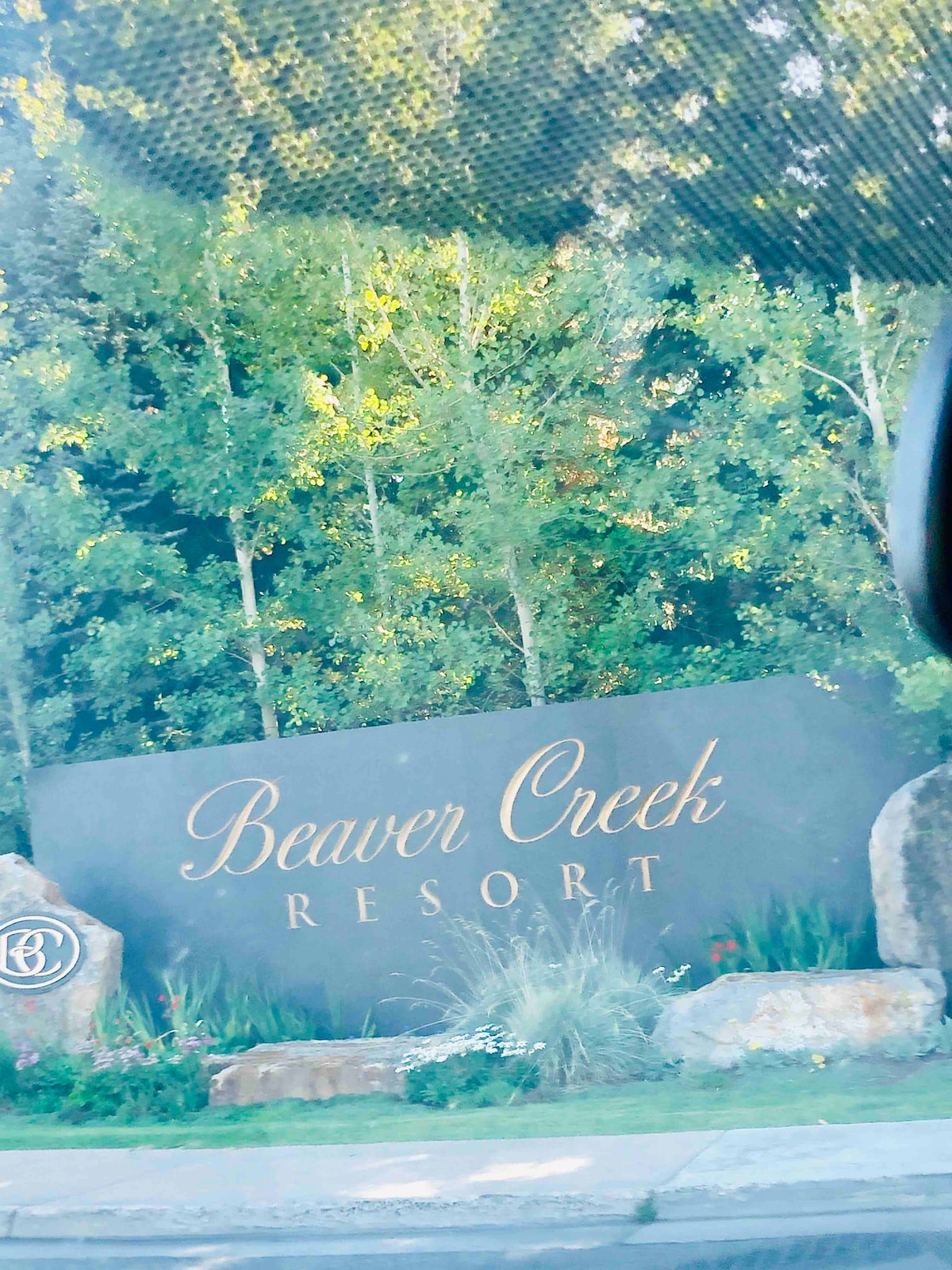 The entrance sign displaying 'Beaver Creek Resort' is framed by lush green trees and natural stone features. The sign is elegantly presented, with gold lettering contrasting against a dark background, inviting guests to explore the resort.