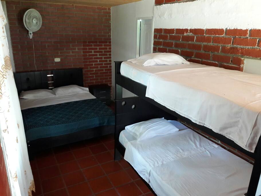 Habitación para 4 personas con baño privado, televisión, ventilador y armario.