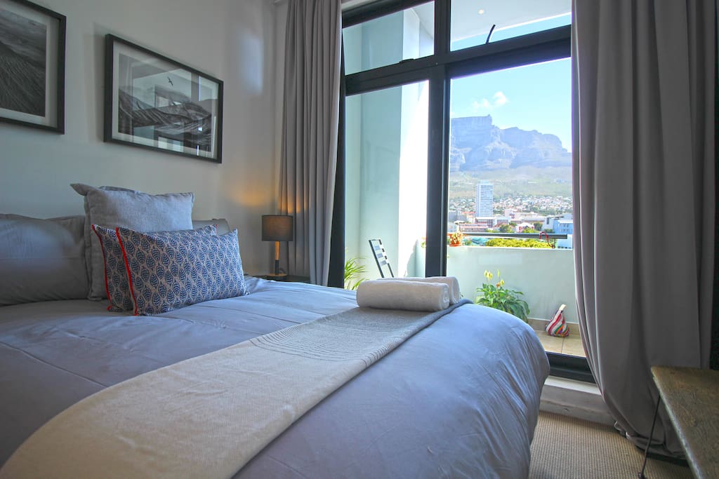 Spacious bedroom with comfortable queen bed, opening to balcony with views of Table Mountain