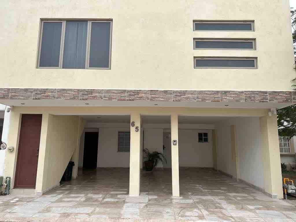 The exterior of the house displays a modern architectural style with a light-colored façade. A spacious driveway leads to a covered garage area, while large windows allow natural light to enter. Simple stone accents enhance the entrance, providing a clean and inviting appearance.