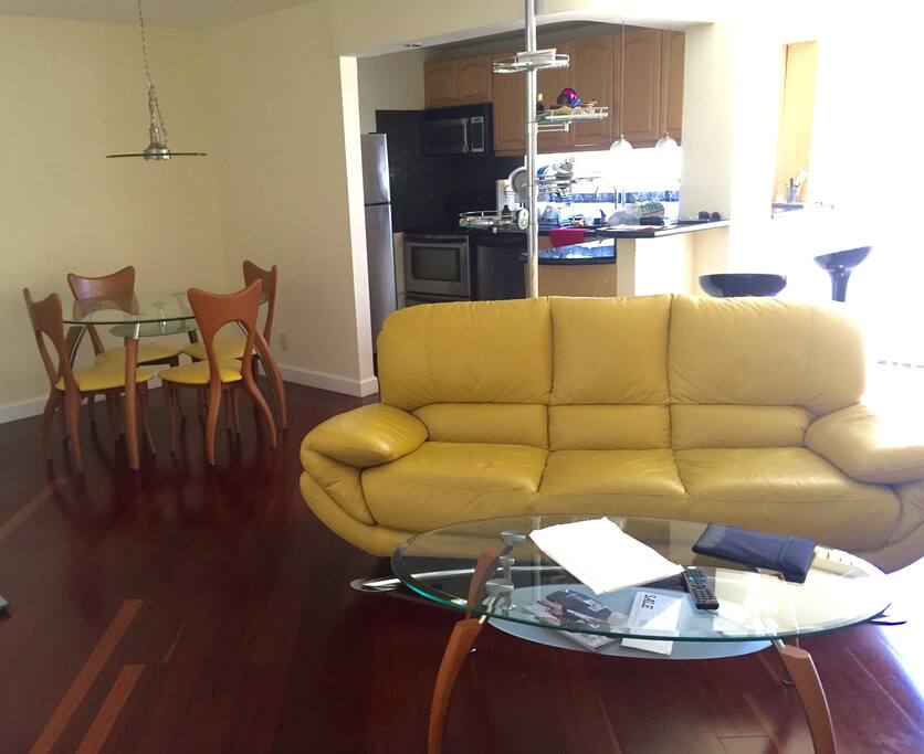 Opened concept kitchen is equipped with microwave, stove, fridge, electric kettle, dishes and silverware.