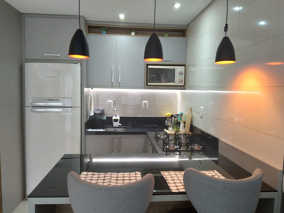 A modern kitchen is presented, featuring a black granite countertop with two upholstered chairs. Pendant lights cast a warm glow over the space, which includes a stove and microwave tucked within sleek cabinetry. A refrigerator is positioned against one wall, enhancing functionality.