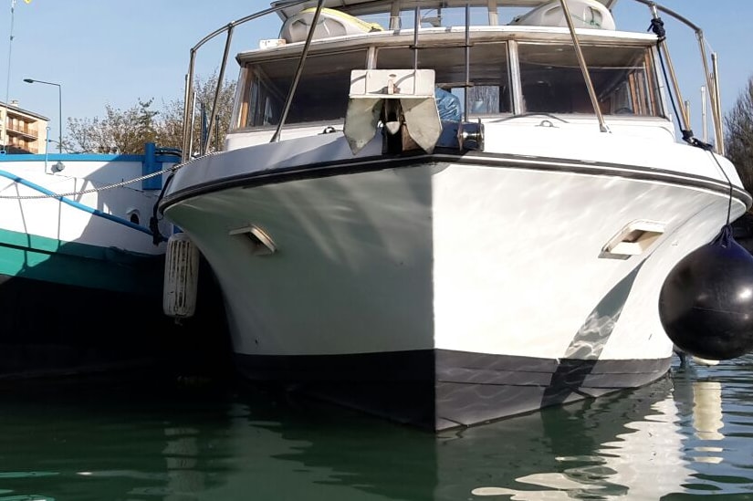 The image features the bow of a charming riverboat, partially moored alongside another boat. The boat's sleek design is highlighted by clean lines and a white hull, with large windows offering views of the interior. The surrounding water reflects a clear blue sky.