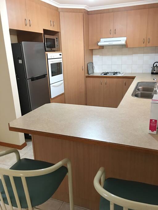 Modern kitchen, fridge, microwave, wall oven, gas cook top, dishwasher. Heaps of dishes and utensils.