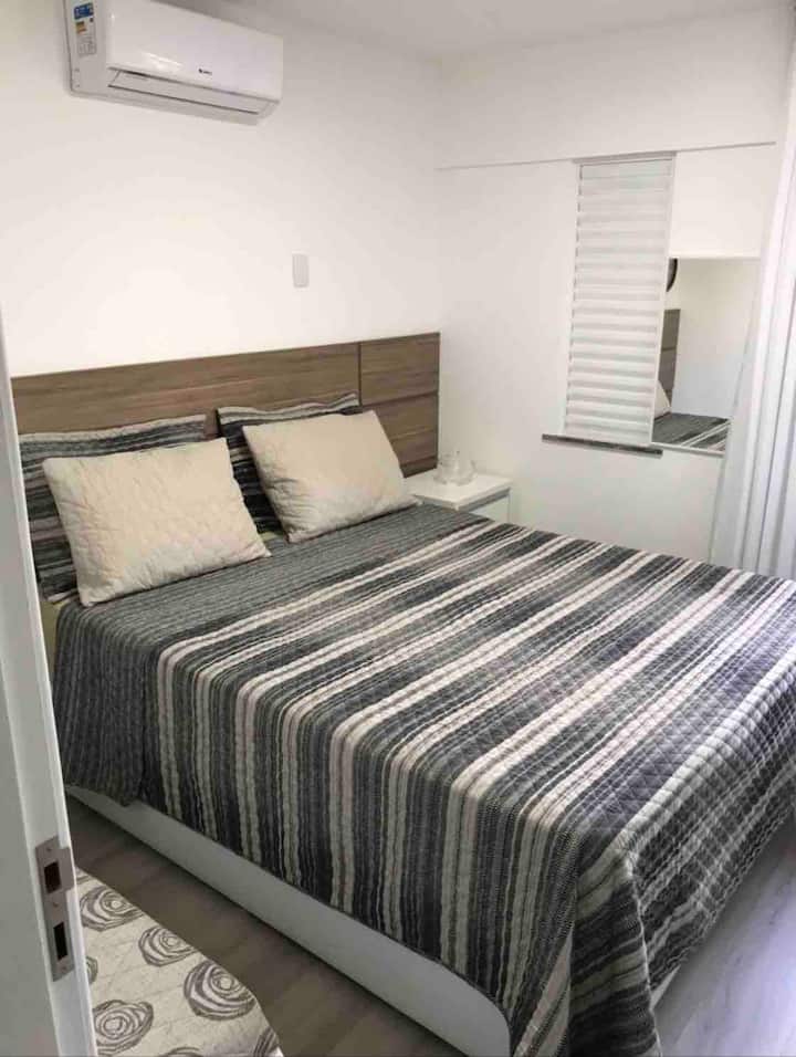 Primeiro dormitório: cama box baú Queen, colchão de espuma ortopédica, ar condicionado split 9.000btus Gree, banco re-camier de apoio, espelho e relógio decorativo de parede.