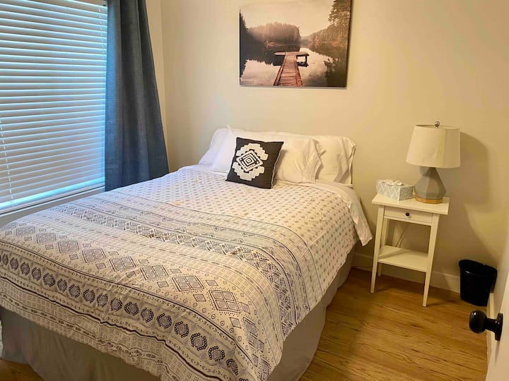 2号卧室位于大厅右侧，设有标准双人床、遮光窗帘、带灯的床头柜和吊扇。