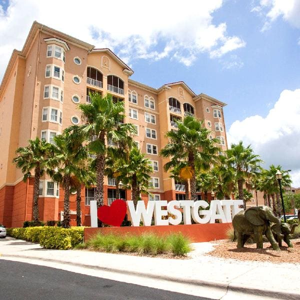 The resort building features a welcoming sign with 'I Love Westgate' surrounded by lush palm trees and neatly arranged landscaping. A playful elephant sculpture is prominently displayed nearby, adding visual interest to the entrance area.