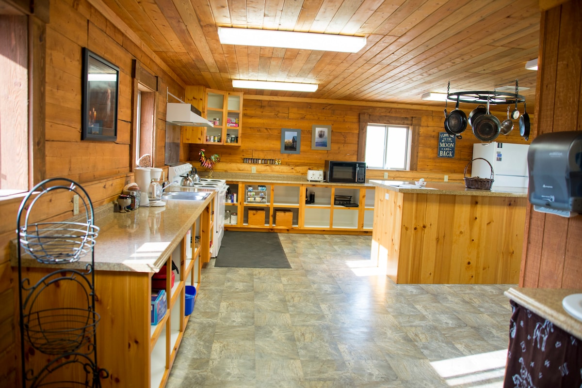 A spacious kitchen is equipped with wooden cabinetry and a variety of appliances, including a microwave and coffee maker. Ample counter space is available for meal preparation, and natural light enters through multiple windows, enhancing the welcoming atmosphere.