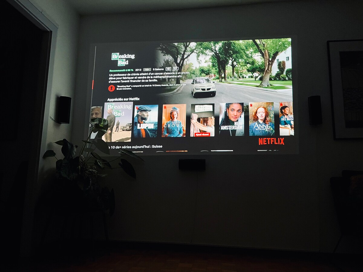 A home cinema projection is displayed on a wall, featuring a menu screen from a streaming service. A peaceful ambiance is suggested by a nearby plant and the soft lighting of the space, creating an ideal setting for a movie night.