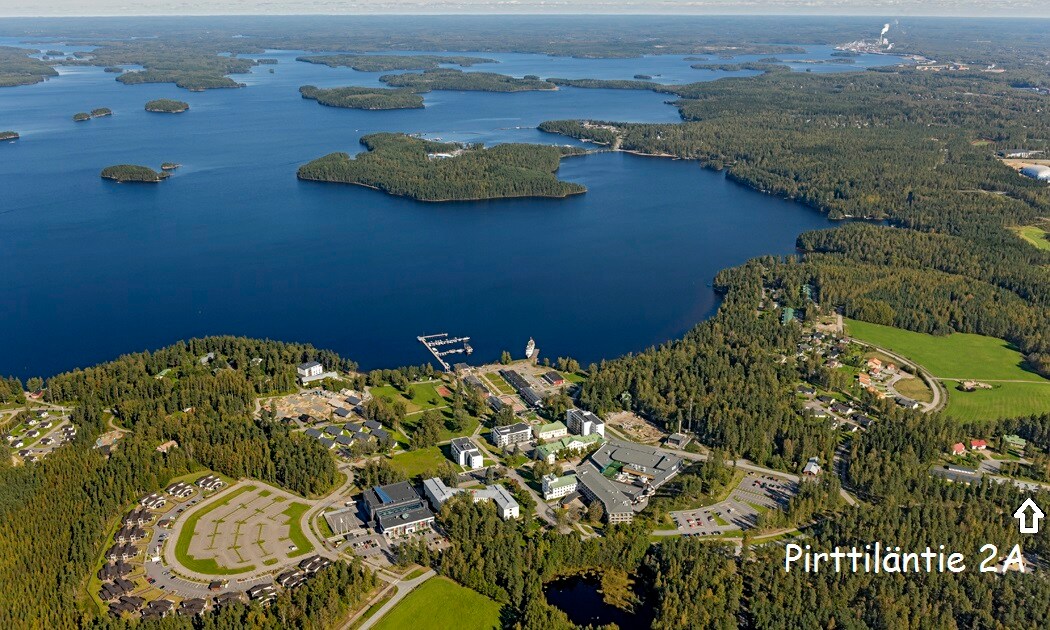 An aerial view displays a vast expanse of water framed by greenery, with numerous islands scattered throughout. The landscape includes a developed area with several buildings and parking spaces, emphasizing the natural beauty of the surroundings.