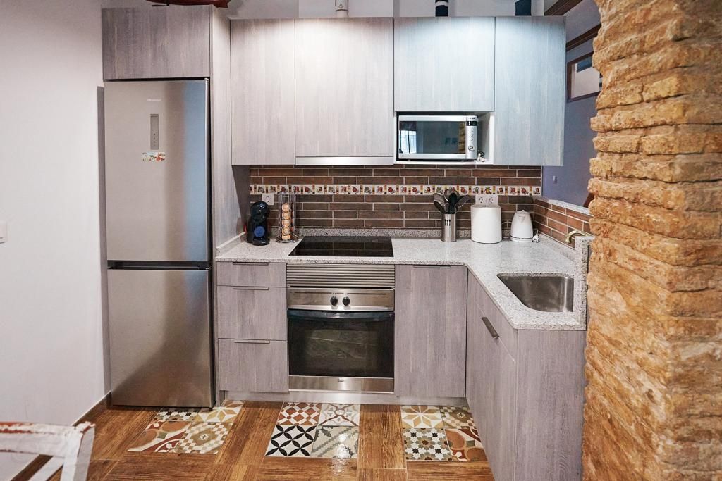 A modern kitchen showcases a blend of grey cabinetry and patterned tile flooring. Equipped with a stainless steel refrigerator, oven, and microwave, it features a granite countertop and a sink, complemented by decorative tiles along the backsplash.
