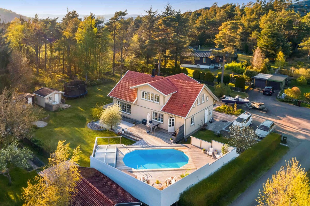 An aerial view of a spacious house surrounded by greenery, featuring a well-maintained garden and a swimming pool. The deck area offers direct access to the pool, while the natural landscape enhances the serene environment.