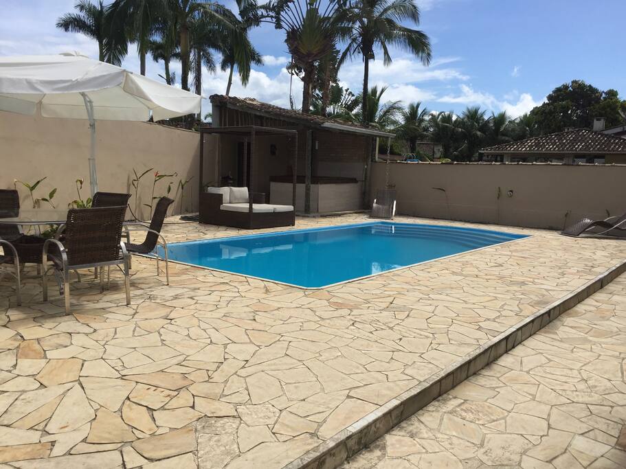 Piscina com escada, mesa para refeição com ombrelone na área externa, bangalô para descanso, espreguiçadeira.