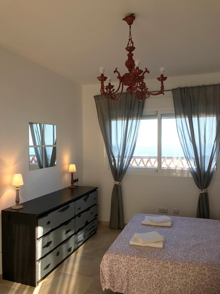 ห้องนอนพร้อมเตียงคู่เตียงโซฟาระเบียงหน้าต่างไปยังระเบียงและวิวทะเล