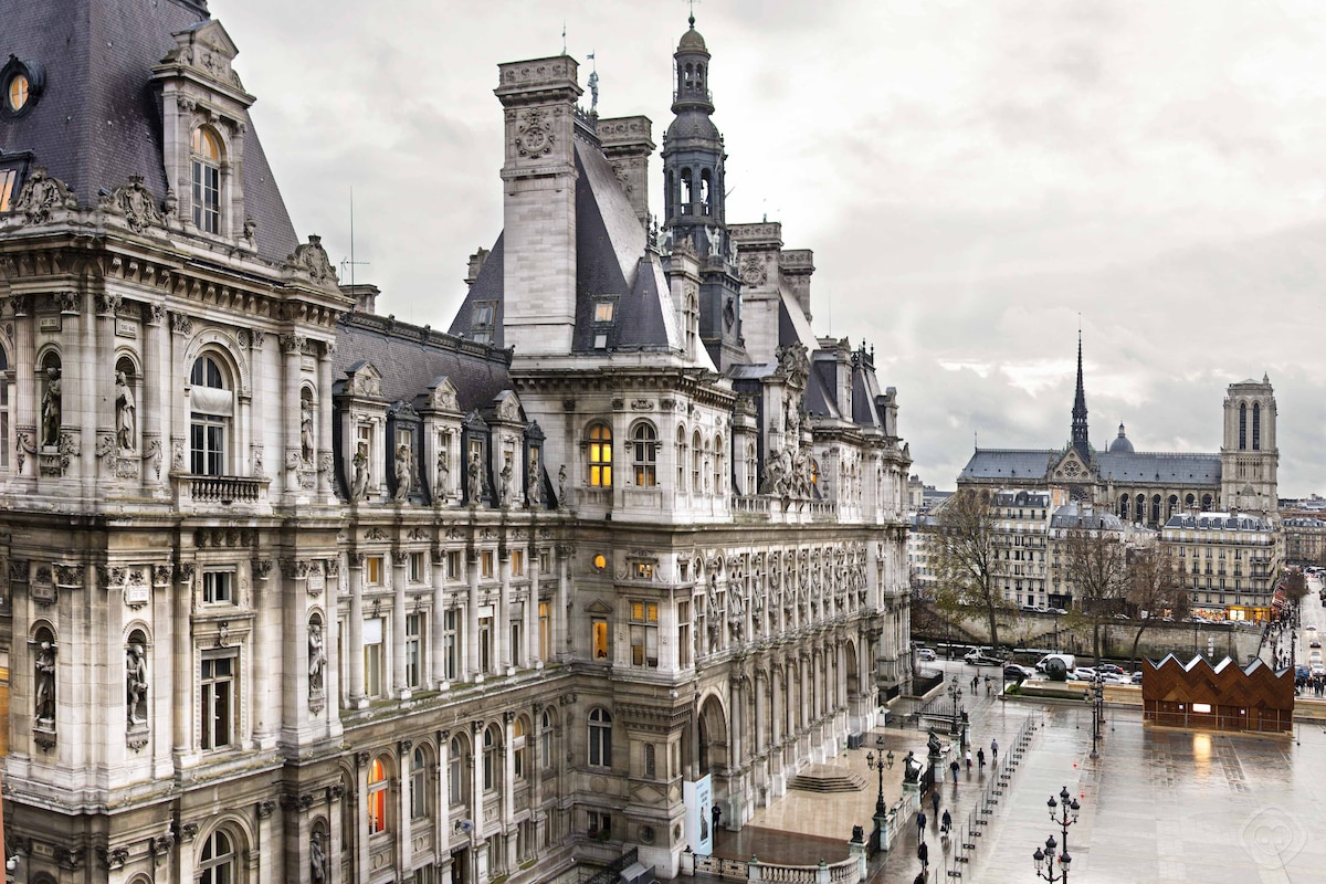 The image captures a historical building with intricate architectural details, viewed from an elevated perspective. The scene includes a prominent spire in the distance, along with hints of modern urban life in the foreground. Soft daylight creates a muted atmosphere, enhancing the classic aesthetics.