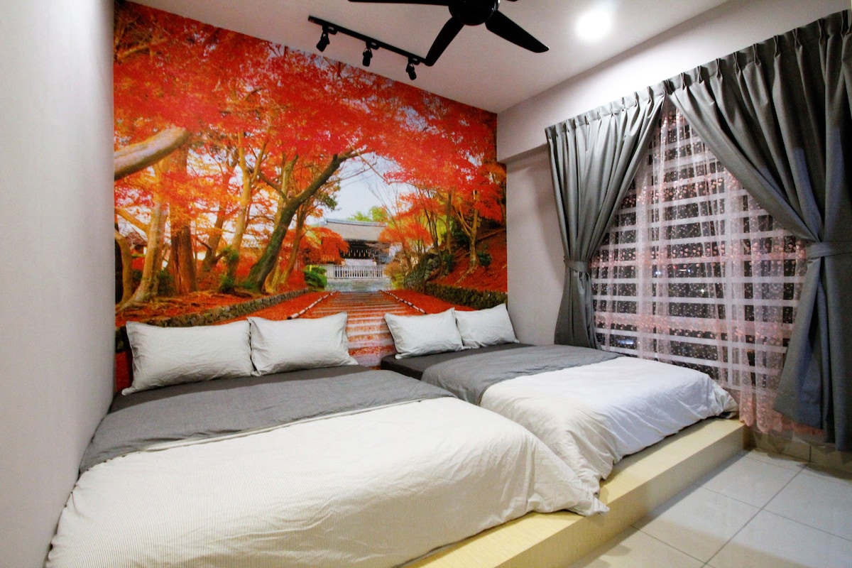 A cozy bedroom displays two spacious beds, each adorned with neutral-colored bedding. The highlight is a striking mural of vibrant autumn trees. Natural light filters through a partially sheer curtain, softening the space and enhancing the warmth of the gray and beige tones.