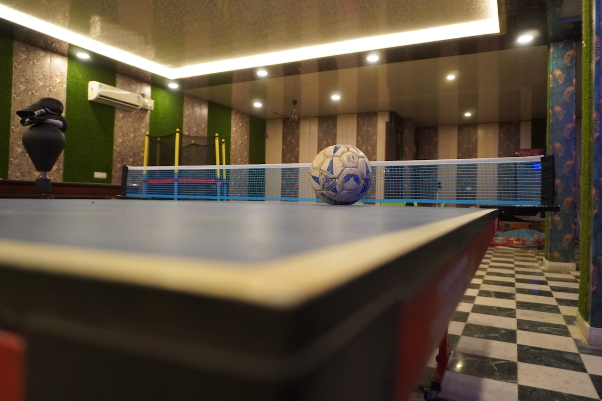 A game room is furnished with a table tennis table and a soccer ball positioned on its surface. The walls are tastefully adorned with patterned wallpapers, and decorative elements such as indoor plants and ambient lighting contribute to the space's lively atmosphere.