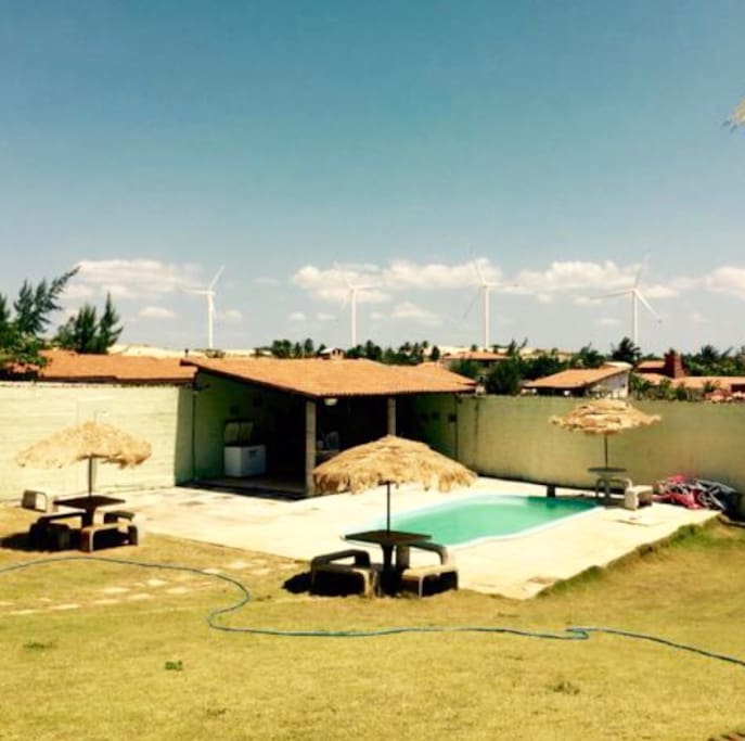 Area do deck com churrasqueira, mesas, cadeiras, freezer, cadeiras de sol e guarda-sois.