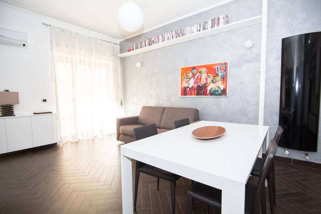 A bright living room with hand-crafted furniture, curved TV, extensible table and a bed sofa