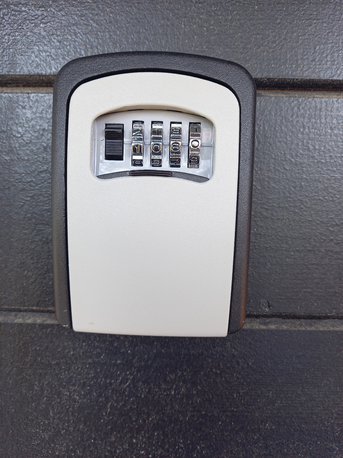 A secure wall-mounted keypad lock is visible, featuring a numeric combination dial. The metal casing is smooth and finished in a neutral color. The lock is positioned against a dark textured surface, providing a clear contrast that enhances its functionality.