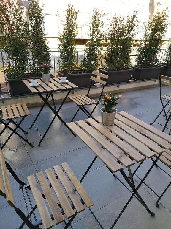 Outdoor seating is arranged on a small terrace, featuring wooden folding tables and chairs. Each table holds a small flower pot, and greenery is placed in long planters along the railing, providing a serene, natural ambiance.