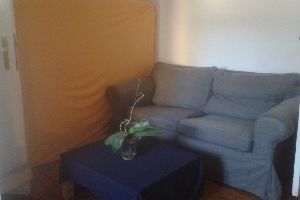 The guest matress with an orange blanket, and the sofa to hang out