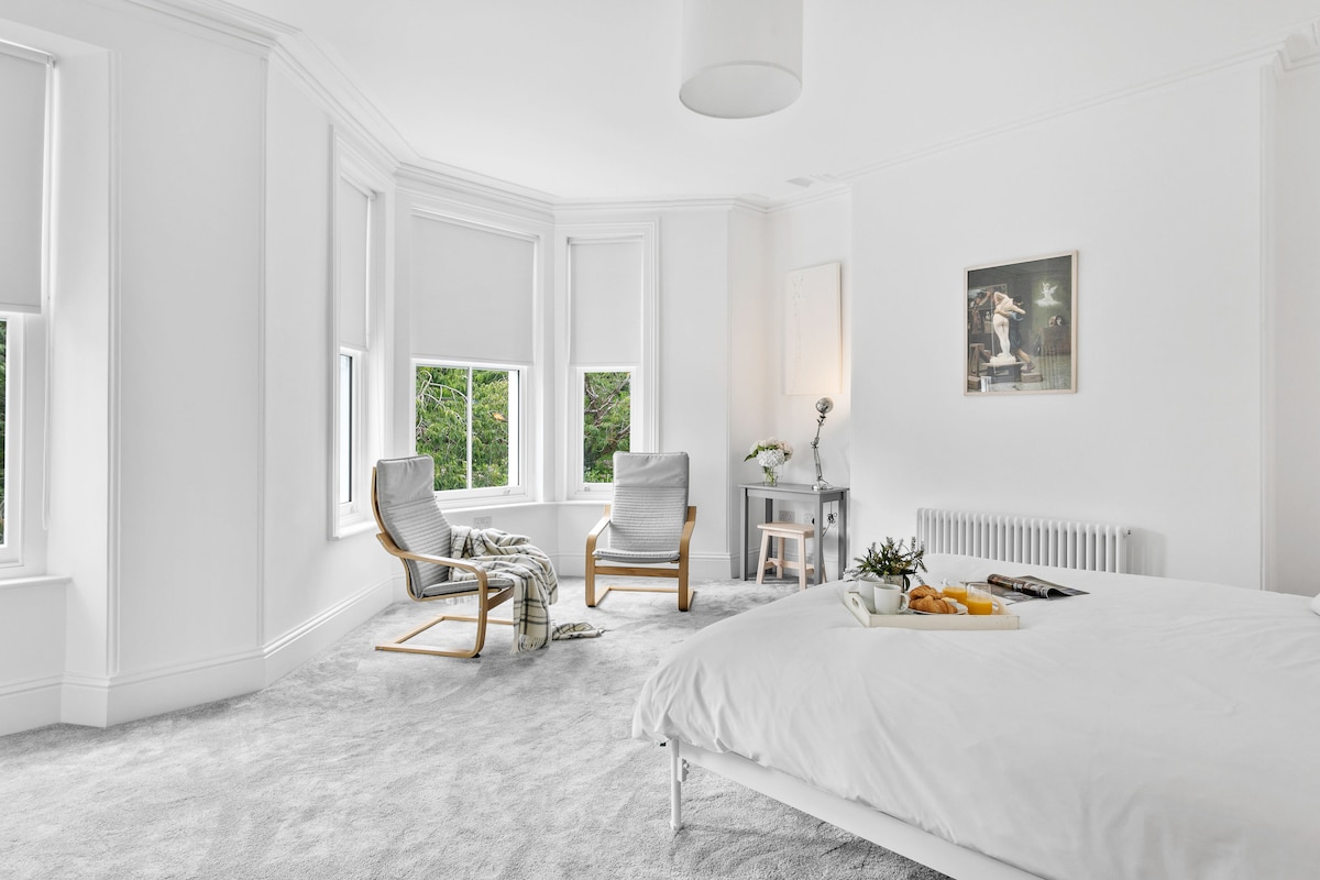 חדר שינה ראשי מרווח עם שטיחון, חלון מפרץ גדול, תריסי האפלה ונוף מרהיב לפארק הו. כולל פינת עבודה, שולחן הלבשה, מיטת סופר קינג ואחסון בשפע.