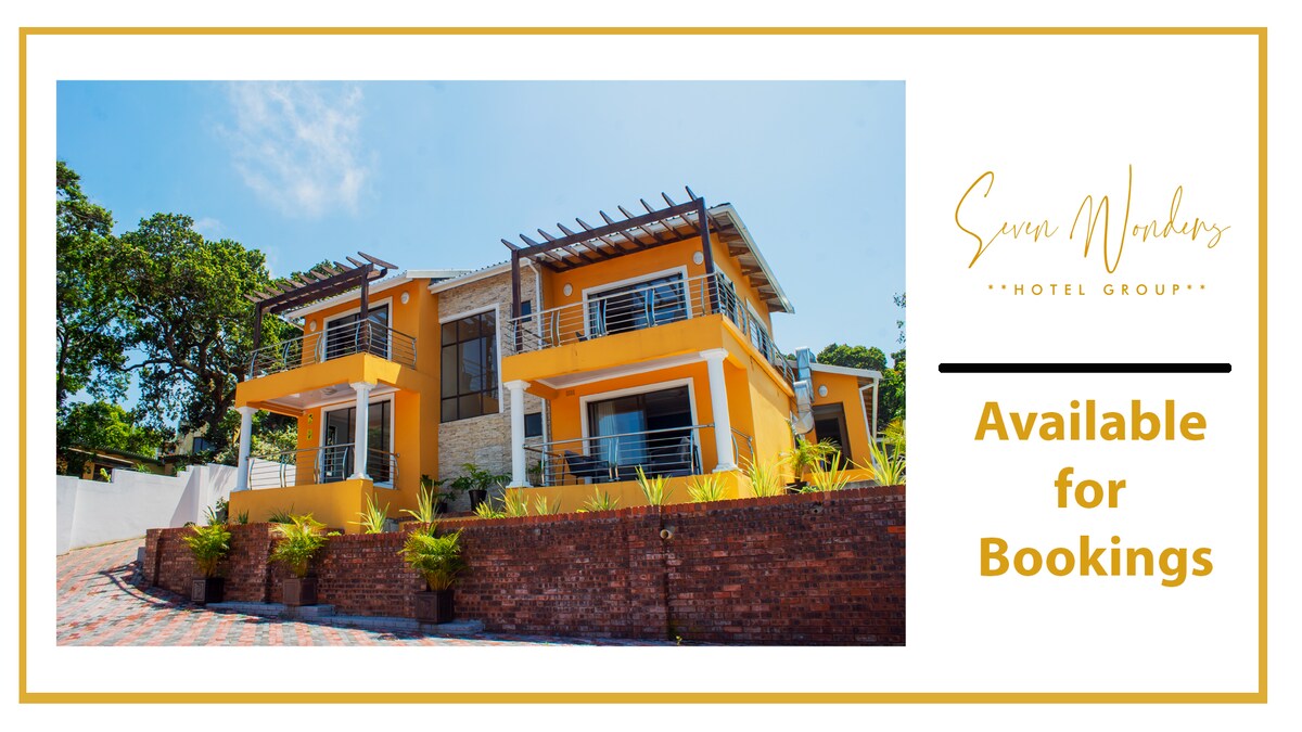 A spacious two-story building is showcased, featuring a bright yellow exterior with modern architectural lines. Large windows and outdoor terraces offer an inviting appearance. Surrounding greenery and a patterned brick pathway enhance the overall setting.