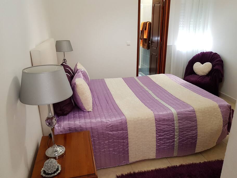 Quarto com cama de casal, TV, mesas de cabeceira, candeeiros, poltrona e roupeiro