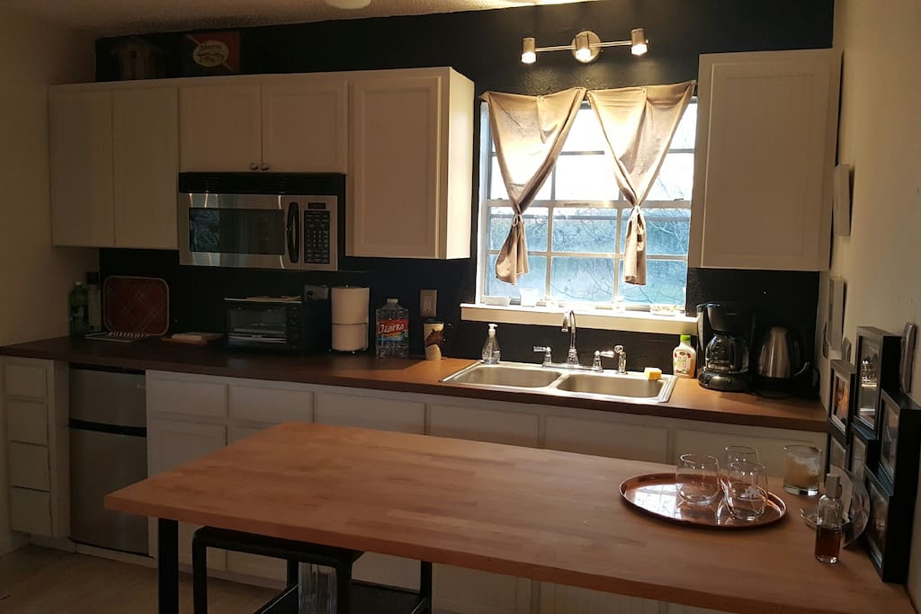 A simple kitchen with small fridge and microwave. Coffee pot, dishes, glasses and utensils.