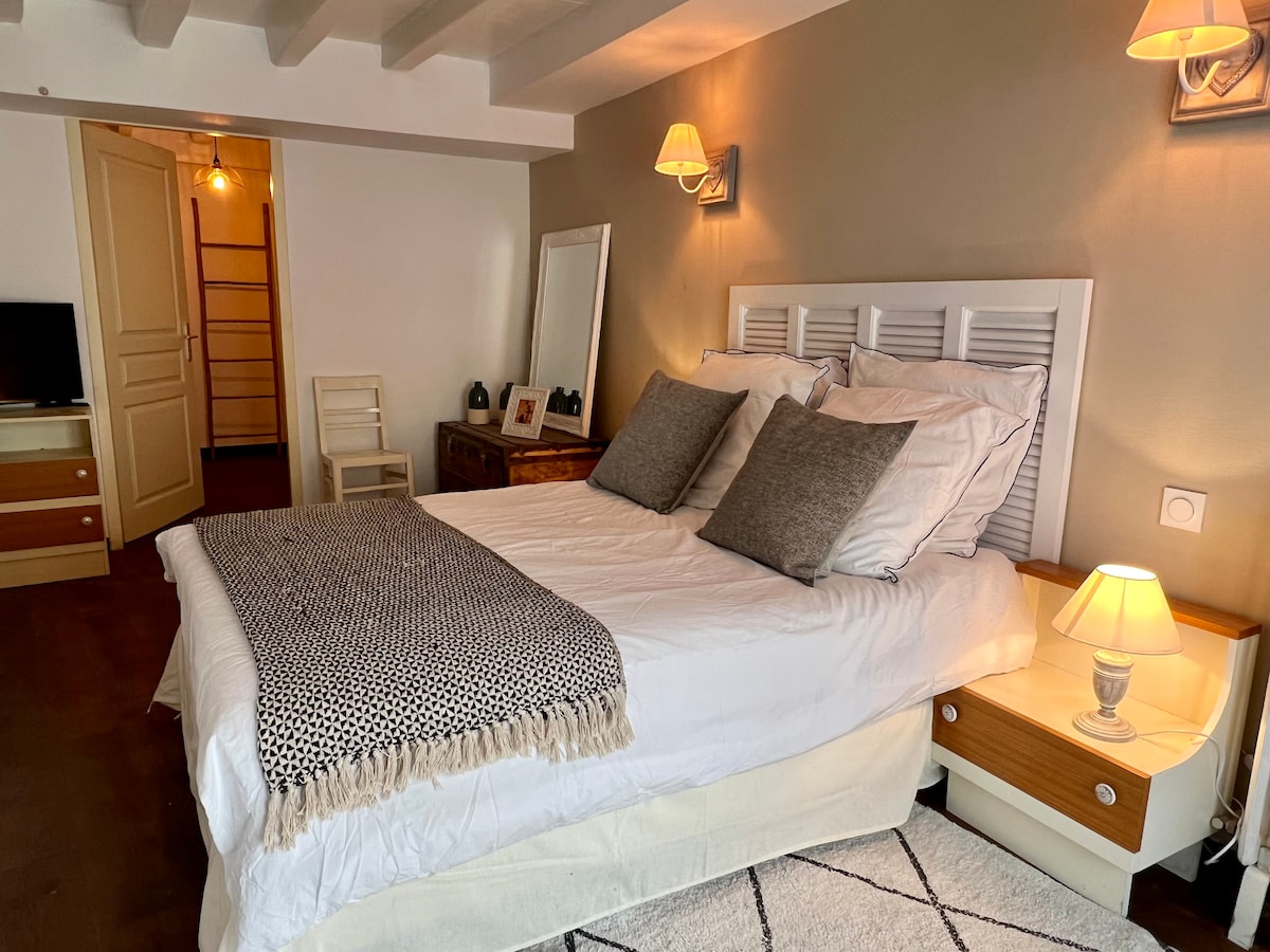 A well-appointed bedroom features a spacious bed with crisp white linens and decorative pillows. Soft lighting from nightstands creates a calming effect. A mirror and a piece of artwork line the walls, while wooden furniture adds warmth to the space.