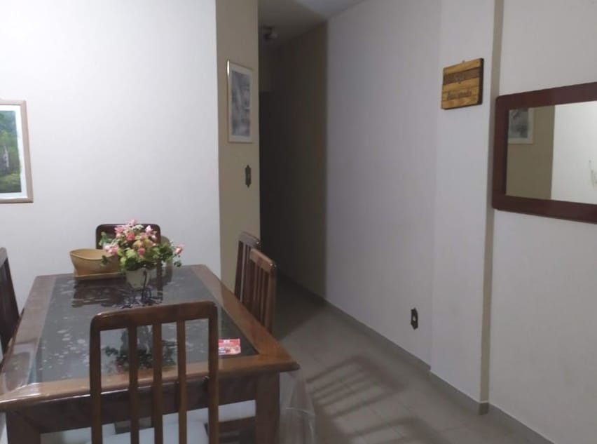 A dining area is presented with a wooden table surrounded by six chairs. A decorative bowl sits at the center, complemented by a small floral arrangement. A mirror is mounted on the wall, and subtle artwork is visible in the background.